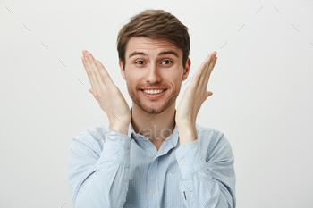 lieved and happy, raising palms near face, smiling broadly and lifting eyebrows in surprise, standing against gray background. Advertisement concept.