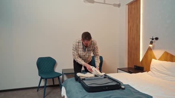 a young man takes out his clothes from a suitcase in a hotel room