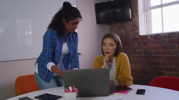 Diverse female business colleagues in discussion at work looking at laptop