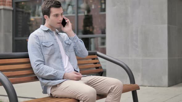 Casual Young Man Talking on Phone Sitting Outdoor