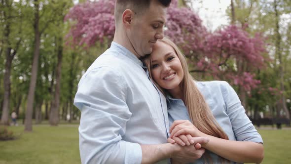 A Couple in Love Stands By a Blossoming Tree and a Tender Young Girl Put Her Head on the Man's Chest