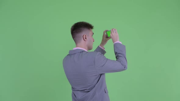 Rear View of Young Businessman Taking Picture with Phone