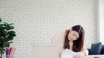 Beautiful young smiling asian woman working laptop on desk in living room at home. / Photodune, Misc