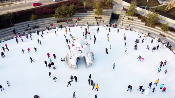 Many People are Skating on White Outdoor Ice Rink in City on Sunny Winter Day