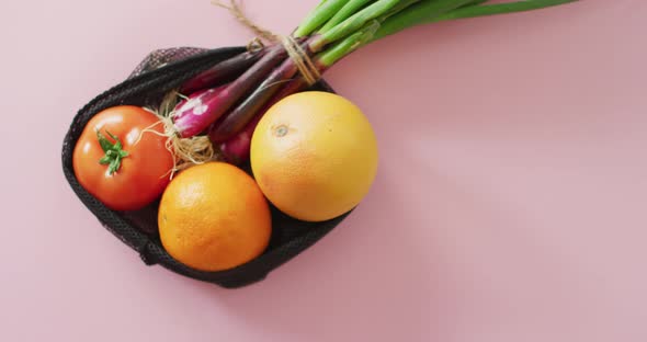 Video of fresh fruit and vegetables in black bag over pink background