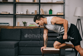 tattooed bi-racial man doing exercise with dumbbell on chair in living room / Photodune, Misc