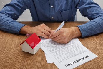 cropped shot of man signing insurance form at wooden table with house model / Photodune, Misc