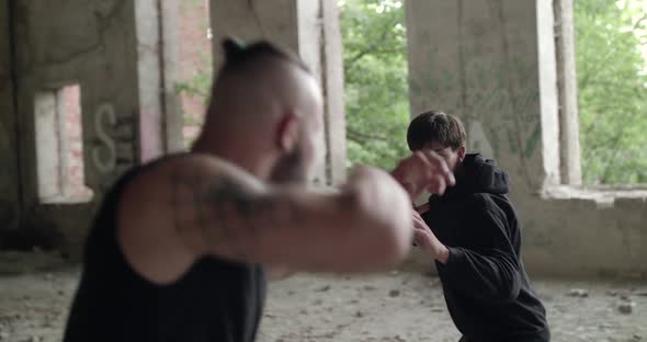 Two Sportsmen Take Attack Poses Before Fighting with Skilled Kicks in Building