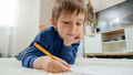 Little boy doing homework in copybook while lying on carpet in living room. Concept of domestic - PhotoDune Item for Sale