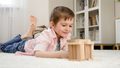Cute smiling boy lying on floor and looking at toy house he built from toy wooden blocks. Concept of - PhotoDune Item for Sale
