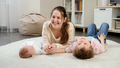 Young smiling mother lying with her little baby and older sons on carpet in living room. Parenting - PhotoDune Item for Sale