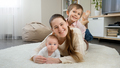 Happy smiling children hugging and having fun with mother on carpet in living room. Parenting - PhotoDune Item for Sale