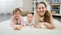 Happy smiling mother with baby and older son lying on soft carpet at living room. Parenting - PhotoDune Item for Sale
