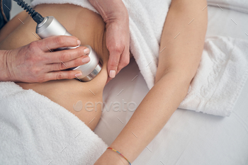 ving towels on her body while cosmetologist applying hand probe to her hip