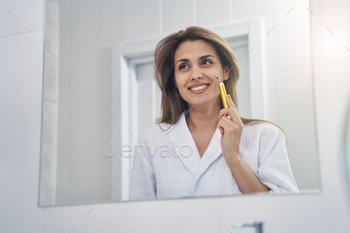 Joyful young woman using golden facial massager in bathroom / Photodune, Misc