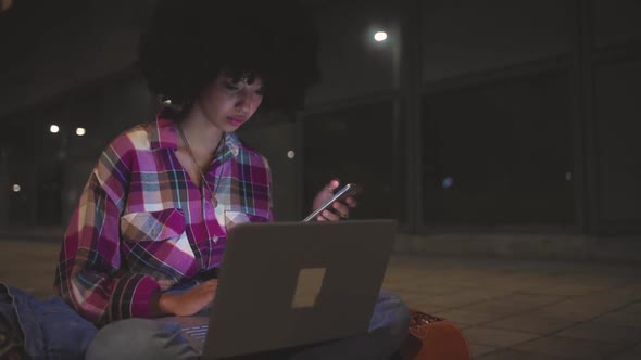 Young woman using laptop and smartphone in the city at night