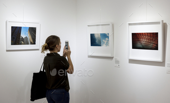 Woman in an art exhibition taking a photo of an art / Photodune, Misc
