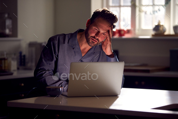 ラップトップを使用して夜にキッチンに座っているパジャマを着ている不幸な男 / Photodune, Misc
