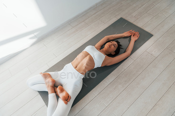 Lying down on the yoga mat. Young caucasian woman with slim body shape is indoors at daytime / Photodune, Misc