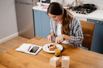 Smiling beautiful woman eating pancakes while having breakfast / Photodune, Misc
