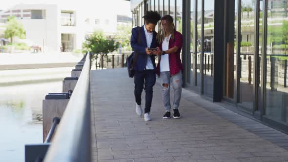 Two diverse male friends walking in the street using a digital tablet