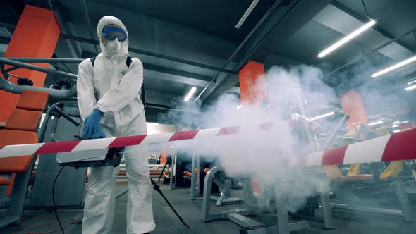 Specialist in a Hazmat Suit Is Fumigating the Fitness Center