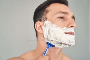 Confident young man shaving beard with a razor / Photodune, Misc