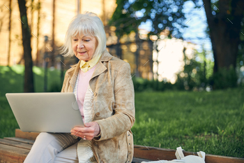 Old thoughtful lady sitting outdoors with laptop during sunny day / Photodune, Misc