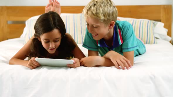 Siblings using digital tablet in bedroom