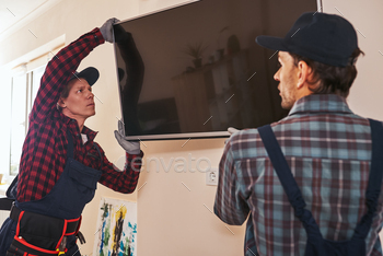 Setting plasma television. Two technician installing television in kitchen / Photodune, Misc