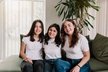 Three pretty smiling caucasian girls in white shirt sitting on the green sofa / Photodune, Misc