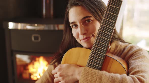 Portrait of Happy Woman with Guitar by Fireplace at Home