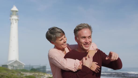 Caucasian couple enjoying free time by sea on sunny day pointing finger