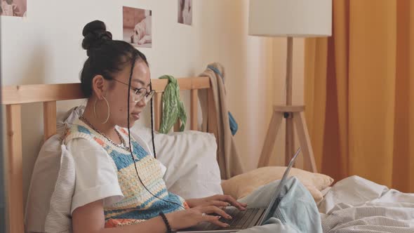 Asian Teenage Girl Typing on Laptop in Bed