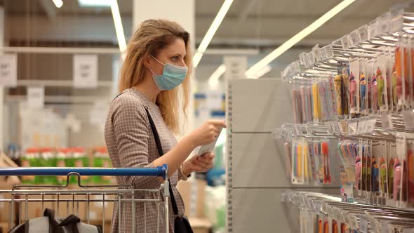 Bayer In Medical Mask In Supermarket Avoid Self Distance. Woman Shopper Choosing Product.