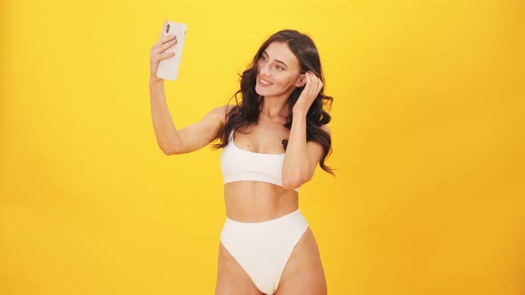 A cheerful brunette woman wearing a swimsuit taking selfie photo using mobile