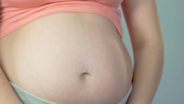 Lady Pregnant with Child Holding Baby Shoes Against Belly, Expecting Daughter