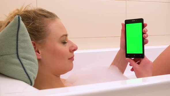 A young beautiful woman looks at a smartphone with a green screen in a bathtub - closeup