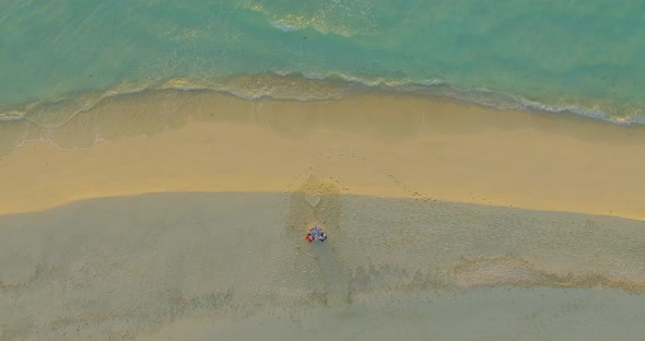 Aerial drone view of a man and woman eating dinner and dining on a tropical island beach