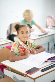 Dark-eyed girl holding pencil while sitting at the desk / Photodune, Misc