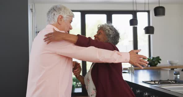 Happy senior diverse couple dancing in kitchen at retirement home