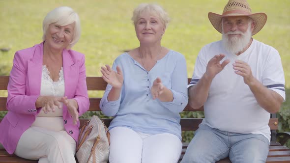 Three Caucasian Middle-aged People Sitting at the Bench and Applauding. Elderly Company Having Fun