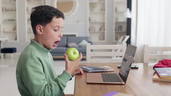 Schoolboy Eating Fresh Apple Near Laptop in Light Room