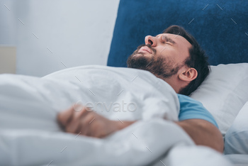 selective focus of grieving man lying in bed and holding blanket / Photodune, Misc