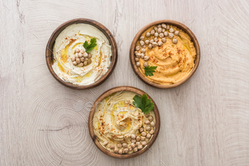 top view of delicious hummus with chickpeas in bowls on beige wooden table / Photodune, Misc