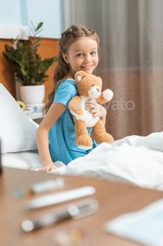 Little patient with teddy bear sitting on bed in hospital / Photodune, Misc