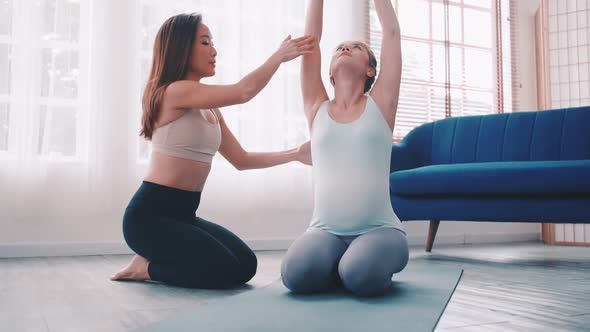 Pregnant woman doing yoga exercise with personal trainer at home.