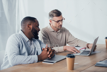businessman using laptop and talking with smiling african american colleague / Photodune, Misc