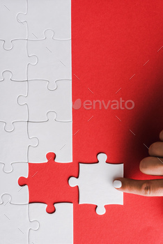 top view of woman pointing with finger at white jigsaw near connected puzzle pieces on red / Photodune, Misc
