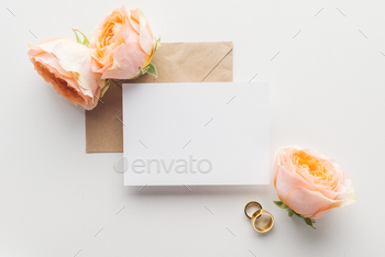 top view of empty card over brown craft paper envelope, roses and golden wedding rings on grey / Photodune, Misc